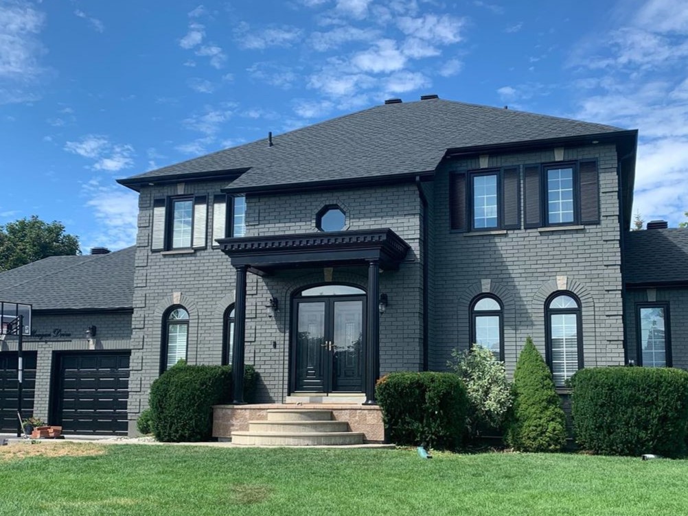 completed paint job of a huge brick house with trim and windows painted black and brick painted grey.