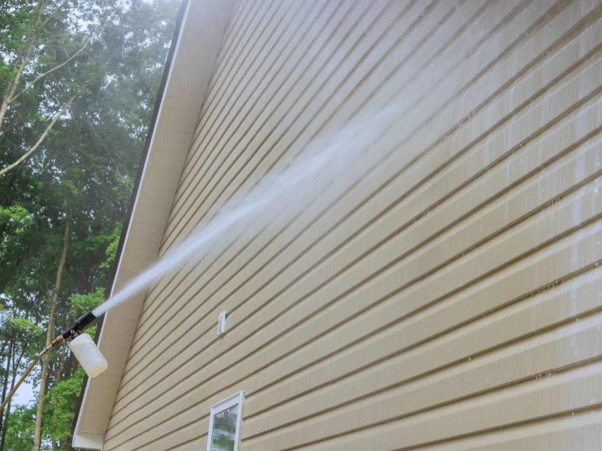 close up of a pressure washing wand cleaning vinyl siding.