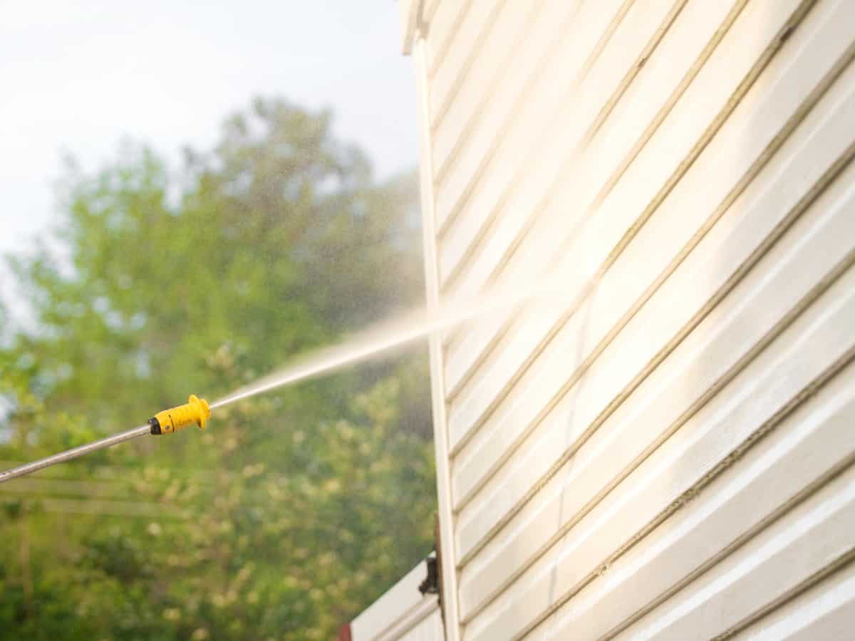 Close up of pressure washing wand cleaning vinyl siding on a house exterior.