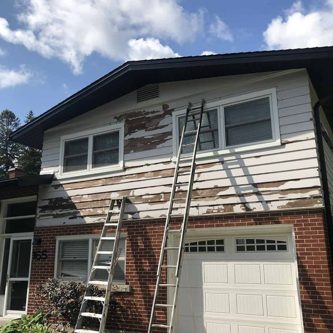 Wood siding being scraped and sanded from ladders in preparation for exterior painting.